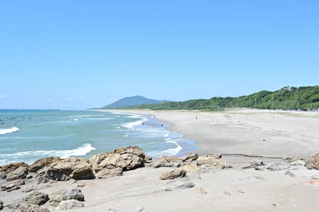 伊良湖ロングビーチの長い砂浜と海、手前の岩場と沖で波を待つサーファー