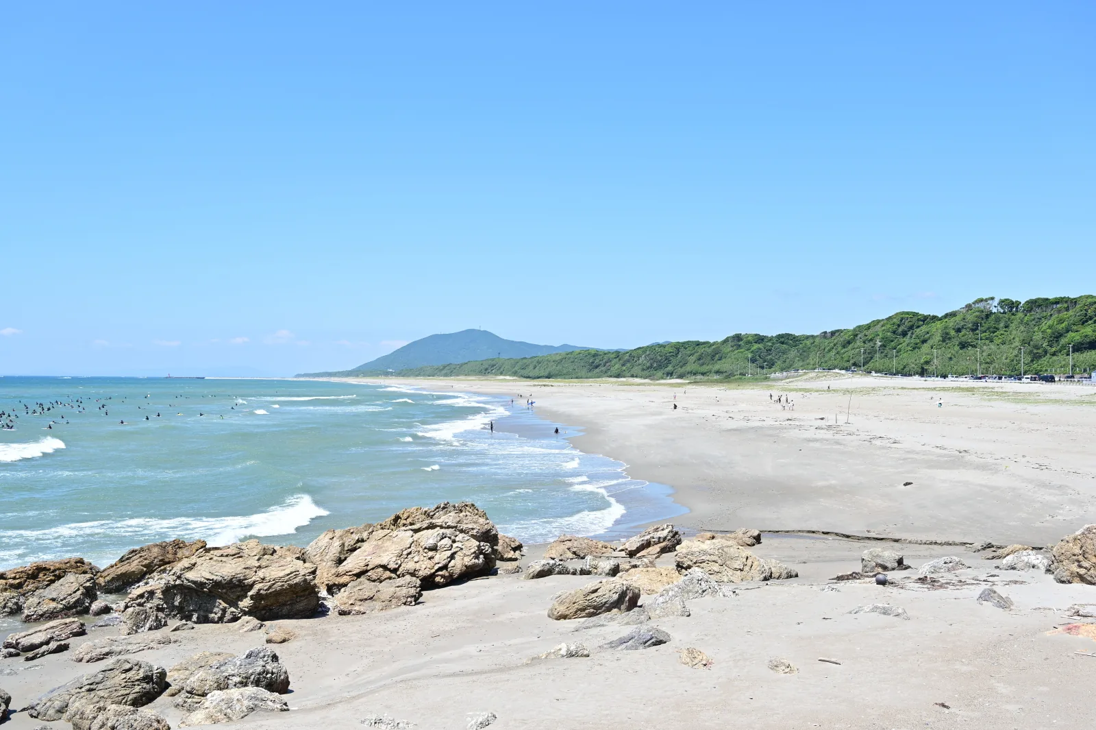 伊良湖ロングビーチの長い砂浜と海、手前の岩場と沖で波を待つサーファー
