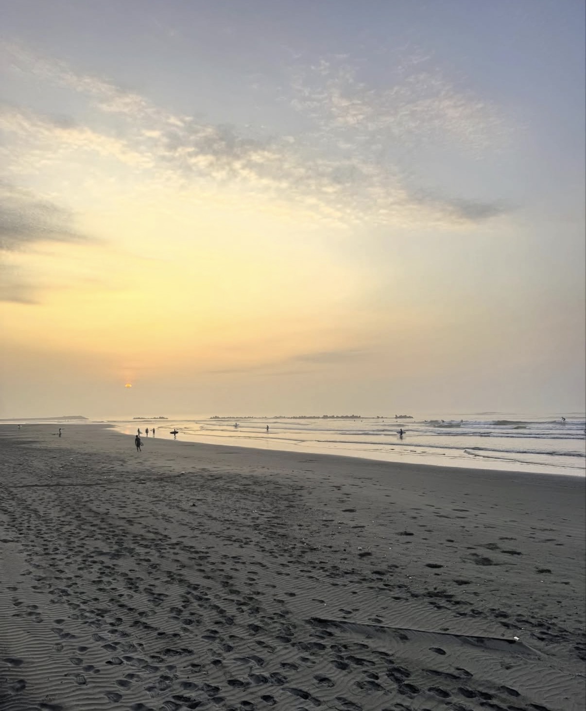 かんぽ前(旧かんぽ下)の砂浜と、柔らかな日差しの海で波を待つサーファー