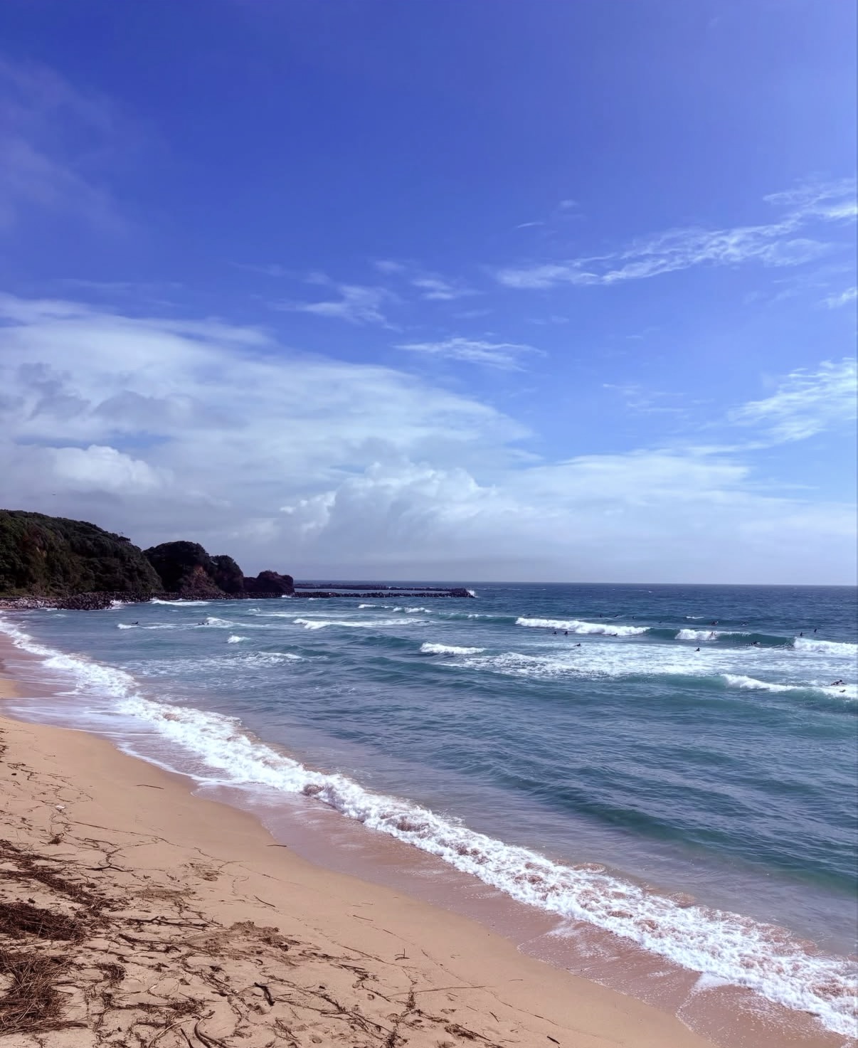 市後浜（いちご浜）の青い海と砂浜に打ち寄せる波、海で波を待つサーファー