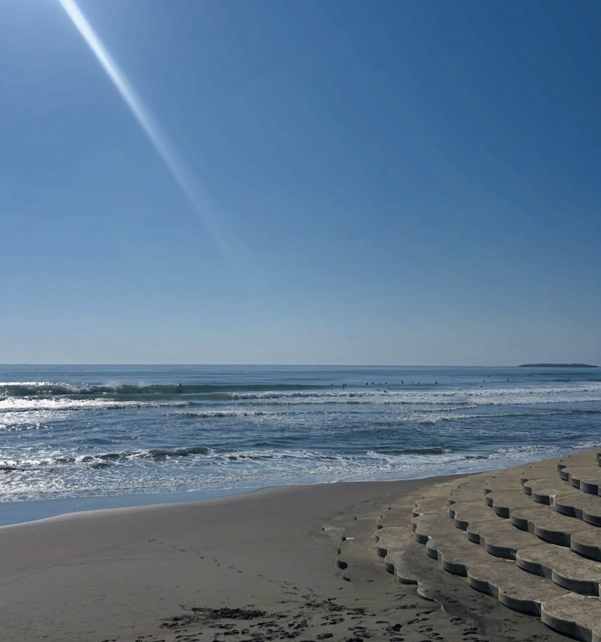 木崎浜の砂浜に打ち寄せる波と、海に入るサーファー