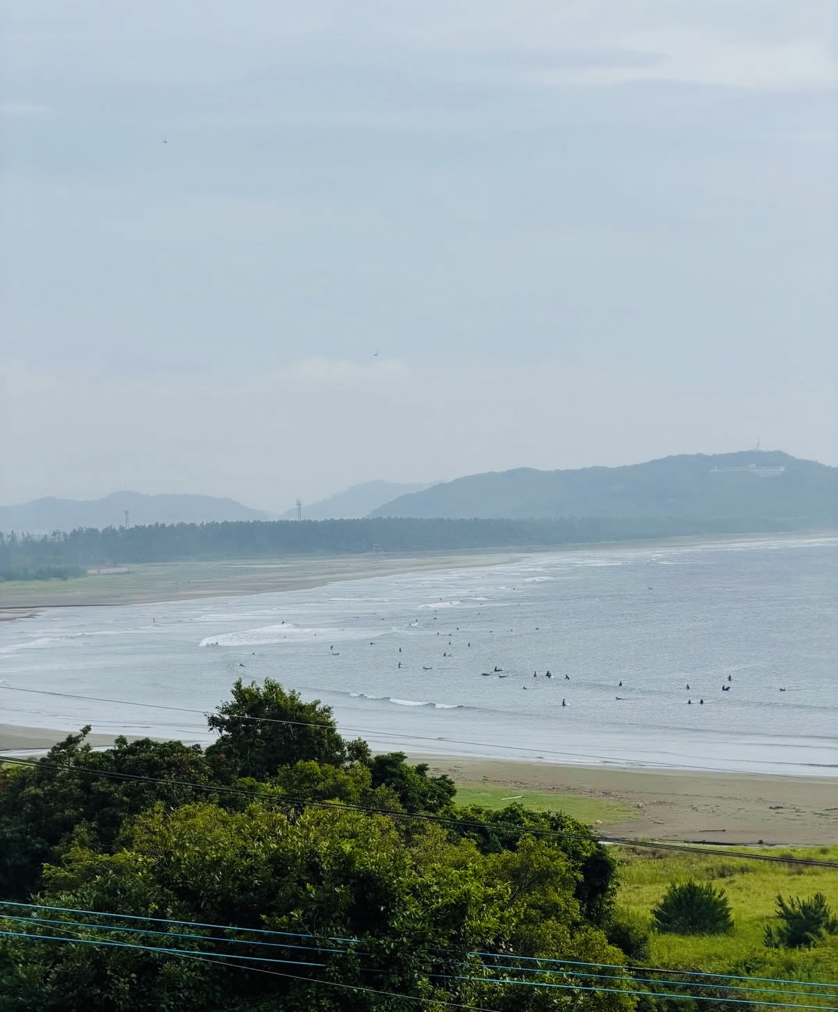 お倉ヶ浜の砂浜と、波を待つサーファーが広がる海岸の風景